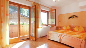 A bedroom with a wooden bed, a large window, and a view of a wooden fence and greenery outside. - Appartment Roswitha (Wagrain)