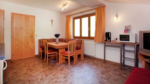 A compact room with a dining table, chairs, a small kitchenette, a television, and a window with curtains. - Appartment Roswitha (Wagrain)