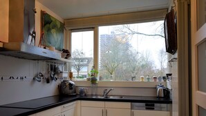 Una cocina moderna con armarios blancos, encimera negra y una ventana con vistas a árboles y edificios.