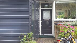 Una casa con una puerta de garaje gris oscuro, una puerta principal negra con un panel de vidrio texturizado, y una ventana que da a la vegetación y flores.