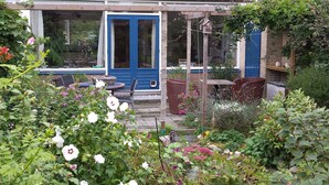 Un jardín con puerta azul, mobiliario de mimbre y diversas plantas.