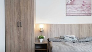 A bedroom with a wooden wardrobe, a bedside table with a lamp, a potted plant, and a bed with grey bedding. - Premium Maisonette Near ski Resorts (Sankt Michael im Lungau)