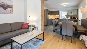 A modern living room with a sofa, coffee table, and dining area. A kitchen is visible in the background with a dining table and chairs. - Premium Maisonette Near ski Resorts (Sankt Michael im Lungau)