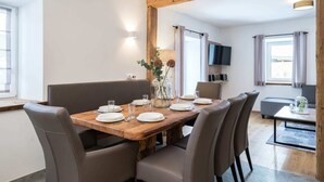 A dining area with a wooden table set for four, surrounded by chairs, a television mounted on the wall, and a window with curtains. - Premium Maisonette Near ski Resorts (Sankt Michael im Lungau)