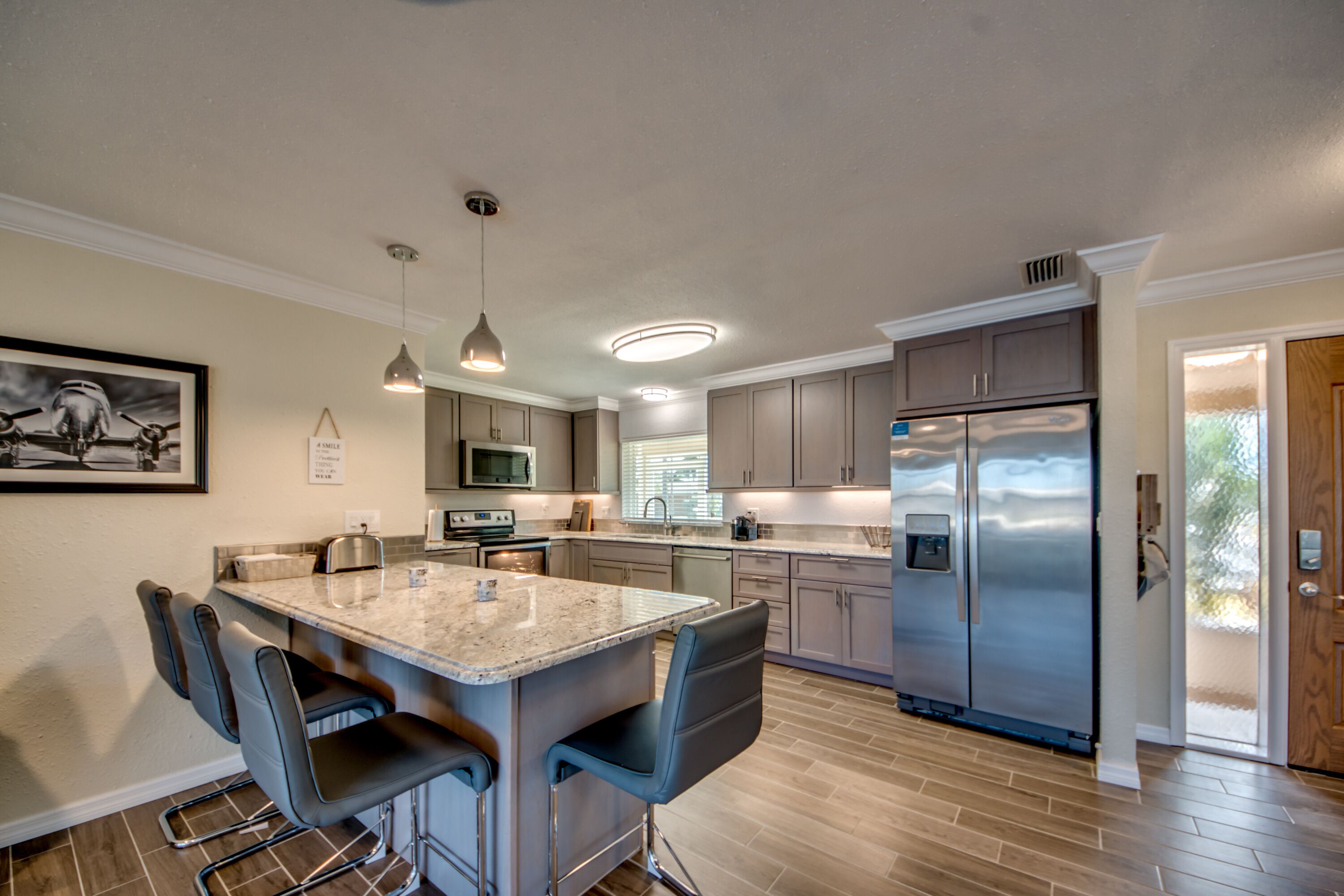 A modern kitchen with a central island, bar stools, stainless steel appliances, and pendant lighting.