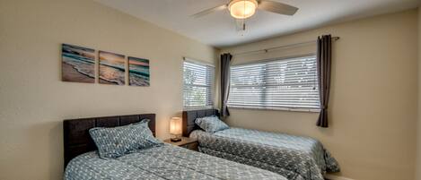 Un dormitorio con dos camas, ventilador de techo y ventana con persianas.