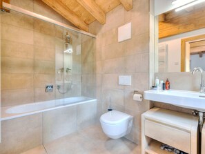 Ein modernes Badezimmer mit einer Duschkabine, einer weißen Toilette und einem Waschbecken mit Pflegeprodukten.