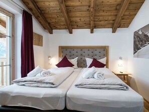 Ein Hotelzimmer mit zwei Betten, Holzbalkendecke, einem Bettkopfteil mit Muster und Blick auf die Berge.