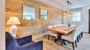 Ein Essbereich mit Holzwand, einem langen Tisch für sechs Personen und einer modernen Kronleuchter.