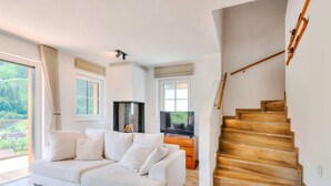 Ein modernes Wohnzimmer mit Sofa, Fernseher, Kamin und einer Holztreppe.