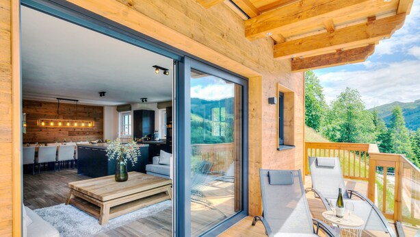 Eine moderne Holz-Blockhütte mit Glastür, die zu einem Essbereich und einem Balkon mit Sitzgelegenheit führt.