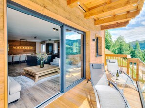Eine moderne Holz-Blockhütte mit Glastür, die zu einem Essbereich und einem Balkon mit Sitzgelegenheit führt.