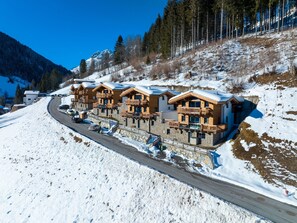 Eine Reihne von Chalets mit Balkonen, gelegen an einem schneebedeckten Hang unter blauem Himmel.