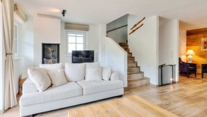 Ein modernes Wohnzimmer mit einem weißen Sofa, einem Holztisch, einem Fernseher und einer Treppe, die zu einer anderen Ebene führt.