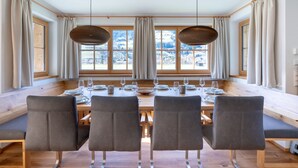 Een eethoek met een lange tafel, vier stoelen en uitzicht op een besneeerd landschap door grote ramen.
