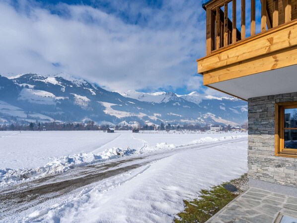 A snow-covered landscape with a wooden building featuring a stone wall and a balcony. - Chalet in Bad Hofgastein Near Ski Slopes (Bad Hofgastein)