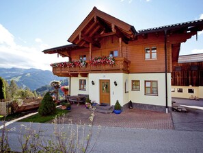 A two-story wooden chalet with a balcony, a wooden fence, and a garden with potted plants.