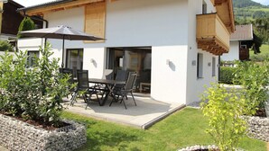 Ein modernes, zweistöckiges Haus mit einer Terrassenfläche, komplett mit Tisch und Stühlen, umgeben von gepflegten Gärten und Blick ins Grüne.