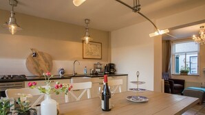 Een moderne keuken met een houten tafel, stoelen en een eethoek. Er is een kookplaat, spoelbak en diverse keukenapparaten.