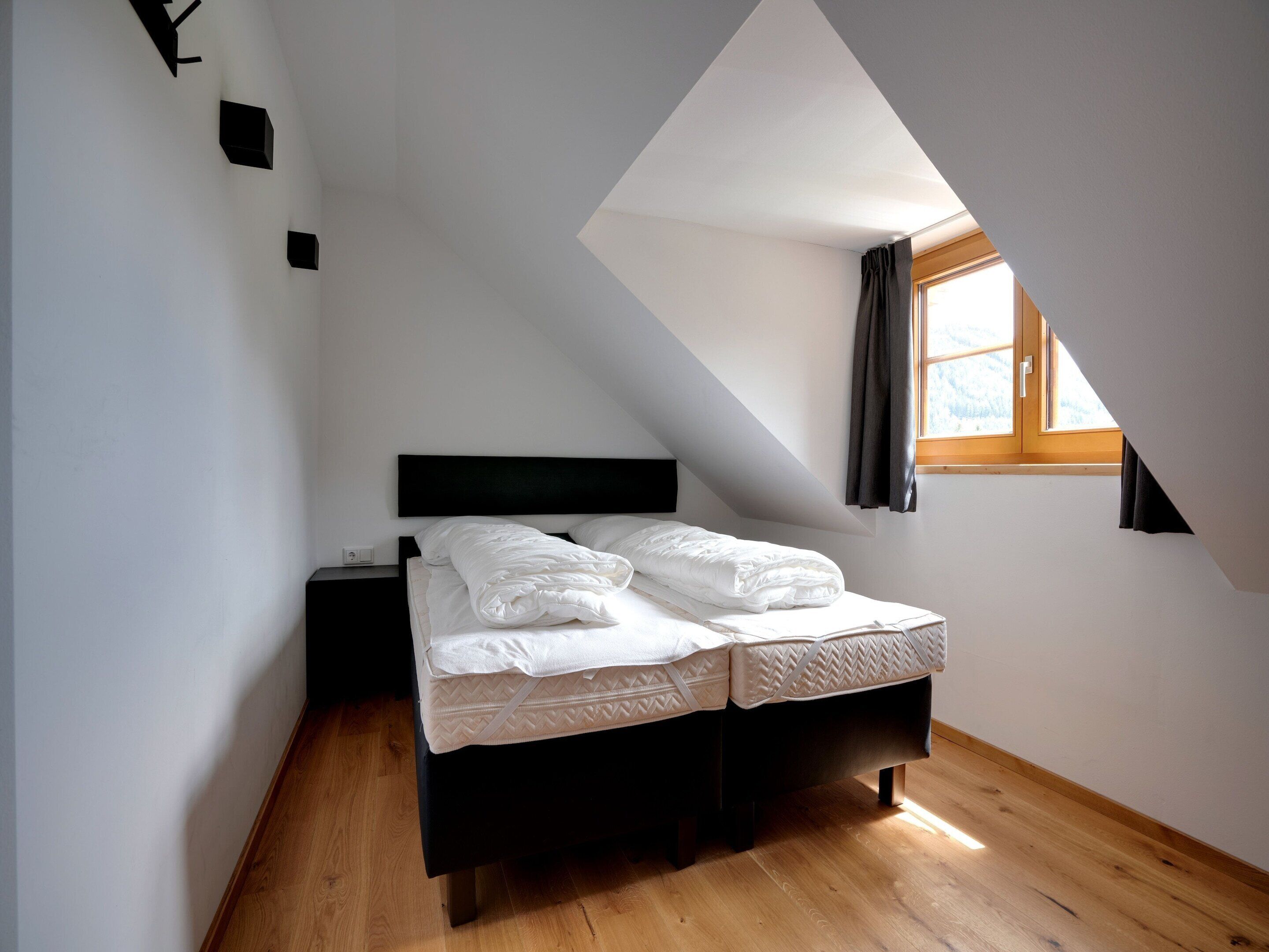 A bedroom with a bed, a nightstand, a window with curtains, and a sloped ceiling.