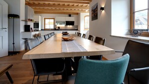 A modern kitchen with wooden beams, a large dining table, and a view of the city through a window. - Chalet in Mauterndorf Near Ski Slopes (Mauterndorf)