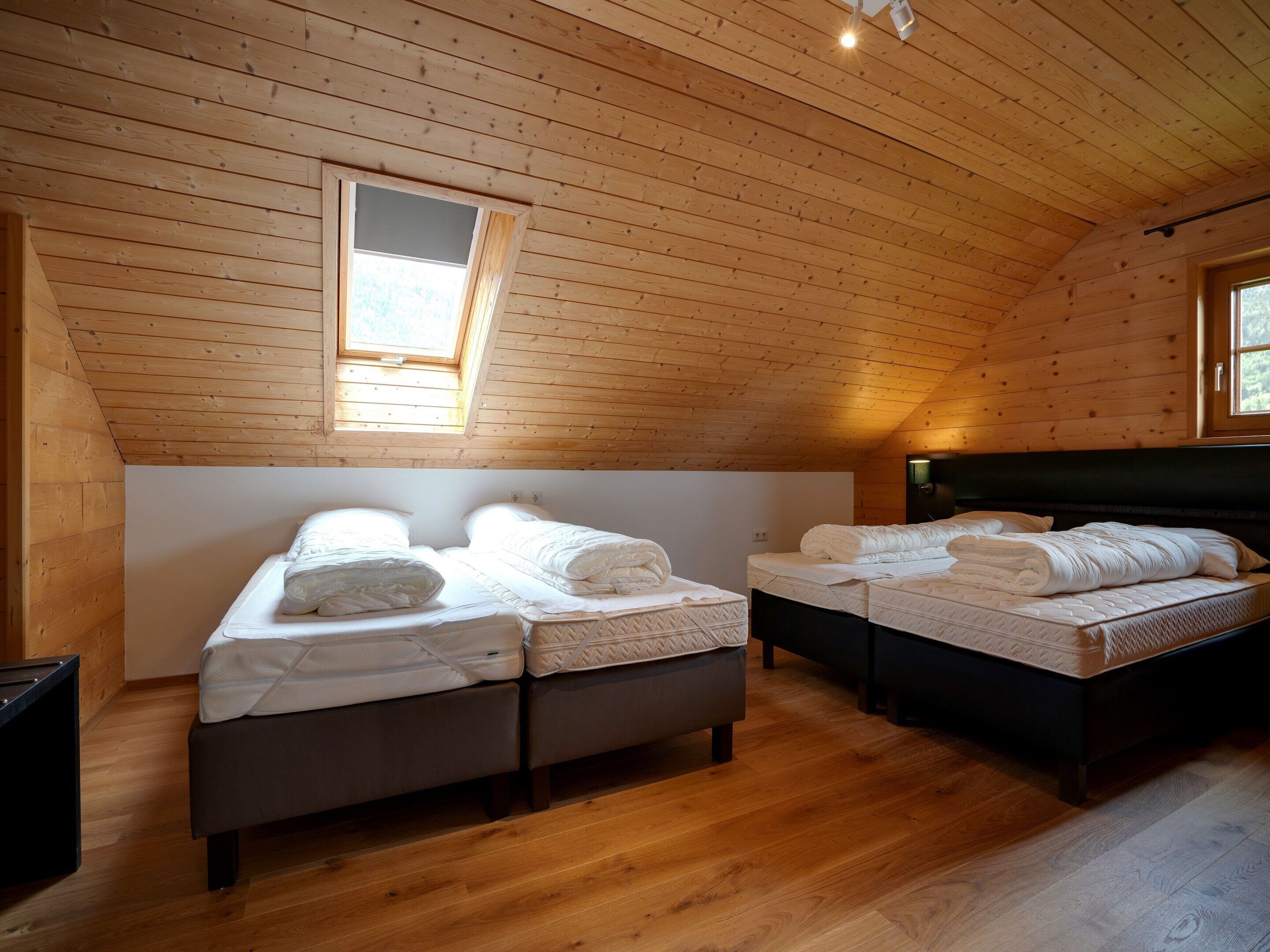 Quarto com duas camas, teto de madeira e um claraboia.