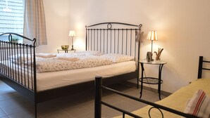 A bedroom with a metal bed frame, a bedside table with a lamp, and a window with curtains. - Apartment in Moselkern in the Countryside (Moselkern)