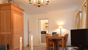 A living room with a wooden cabinet, a dining table with chairs, a TV, and a lamp. - Apartment in Moselkern in the Countryside (Moselkern)