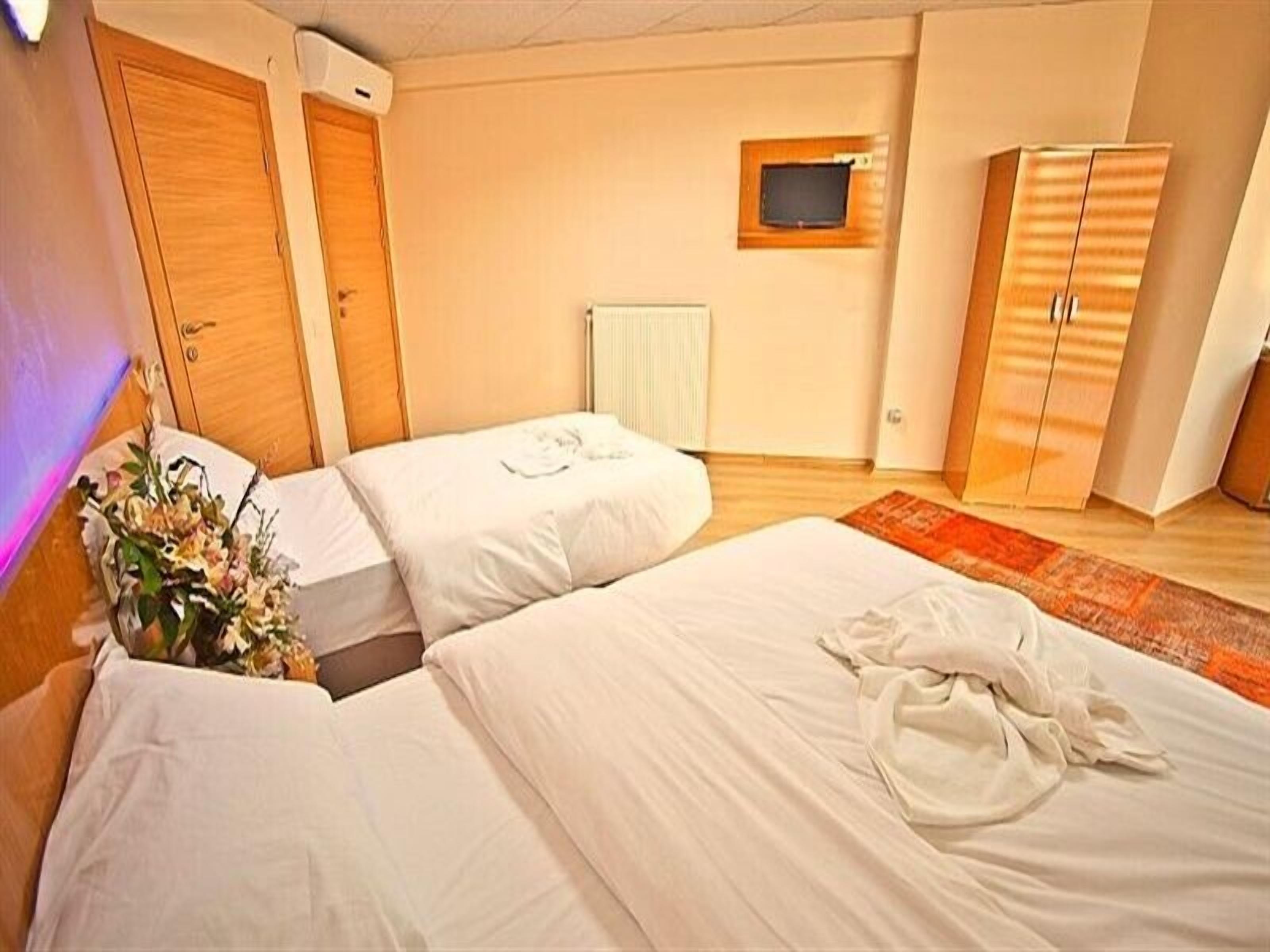 Una habitación de hotel con dos camas, un armario de madera, un televisor pequeño y un radiador.