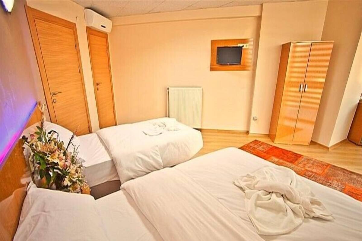 A hotel room with two beds, a wooden wardrobe, a small TV, and a radiator.