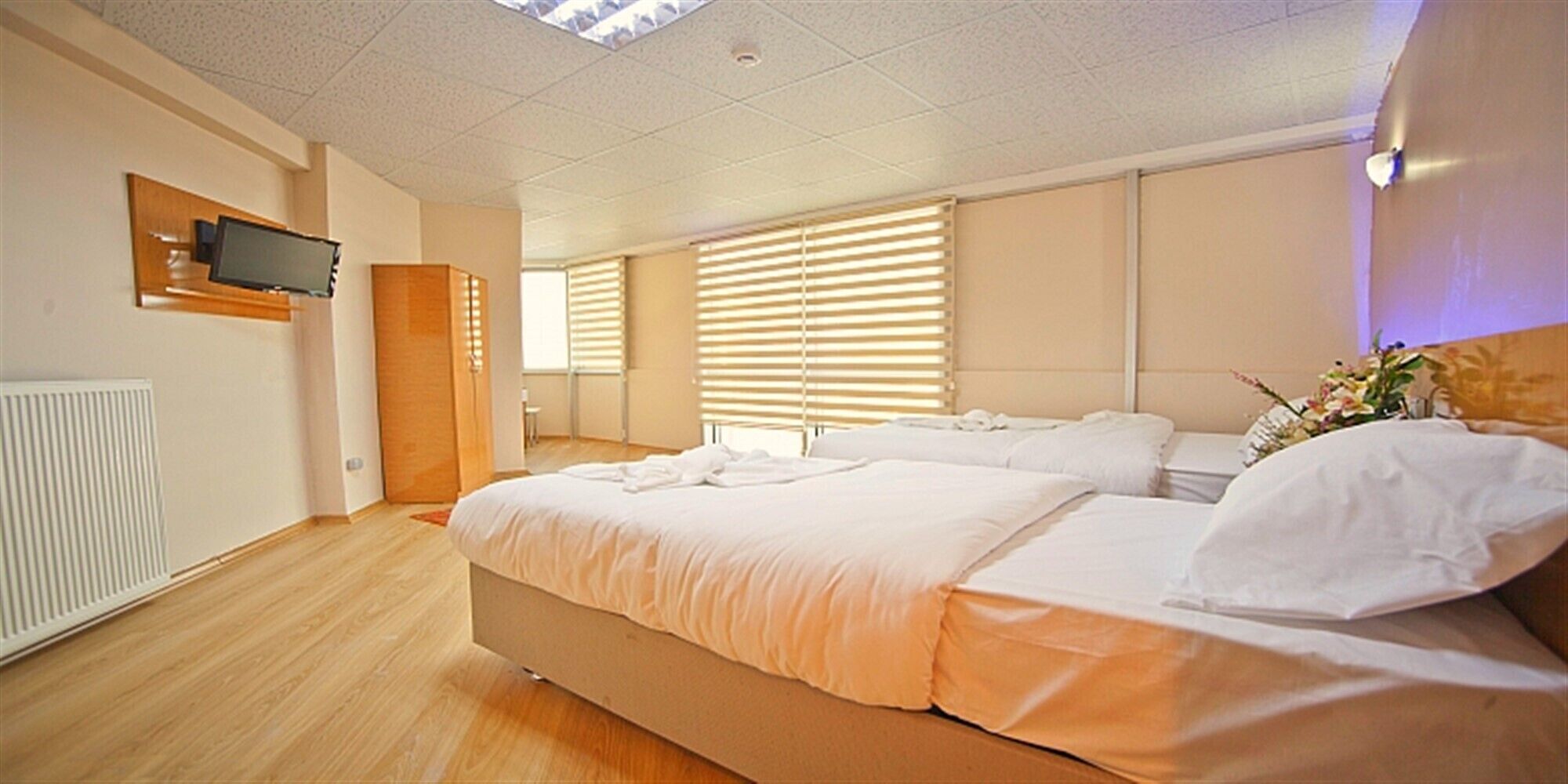 Una habitación de hotel moderna con una cama grande, un televisor montado en la pared y una ventana con persianas.