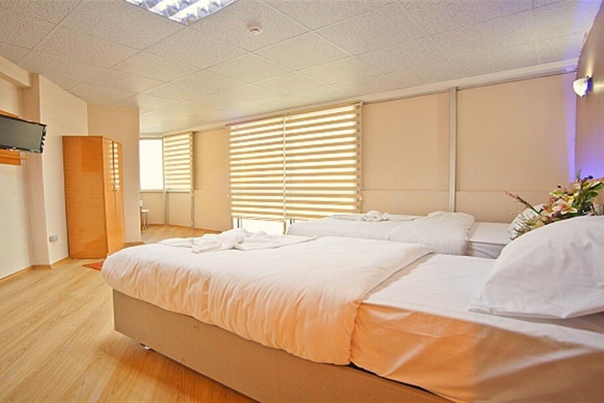 A modern hotel room with a large bed, a TV mounted on the wall, and a window with blinds.