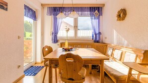 A dining area with a wooden table and bench seating, a window with purple curtains, and a view of the outdoors. - Apartment in Marktrodach With Sauna & Garden (Marktrodach)