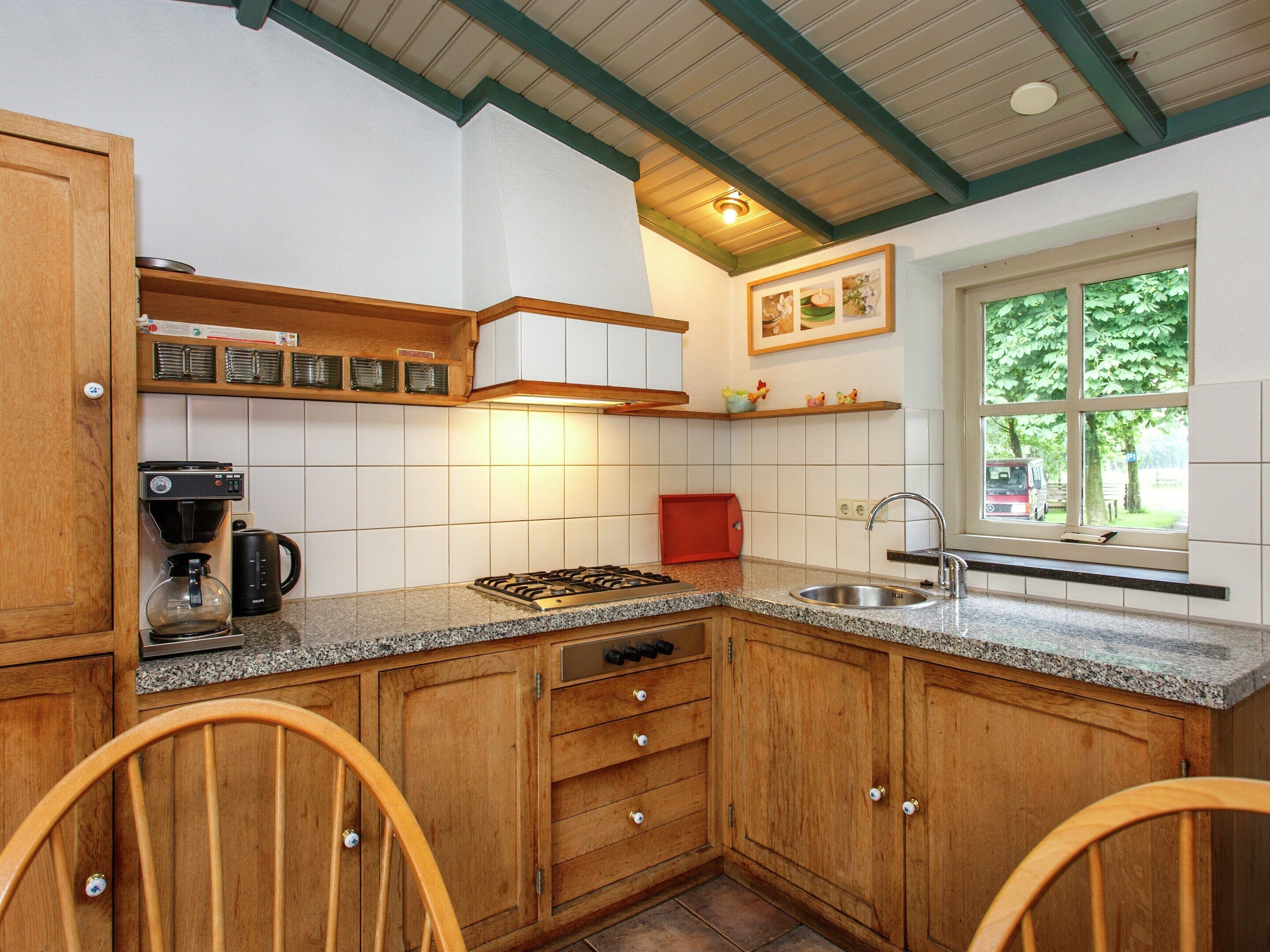 Uma cozinha com armários de madeira, fogão a gás, cafeteira e janela com vista para árvores.