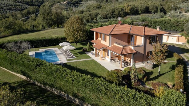Una casa a due piani con piscina, immersa nel verde e circondata da colline.