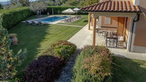 Area piscina con lettini, patio con tavoli e sedie, e vista sul paesaggio circostante.