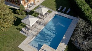 Una vista aerea di una piscina con lettini e ombrelloni, immersa in un prato curato e alberi.