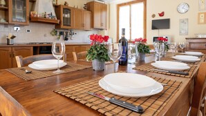 Un tavolo imbandito con piatti, posate e bicchieri da vino, circondato da sedie, in una cucina con mobili in legno e una televisione appesa al muro.