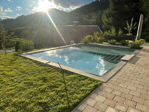 A rectangular swimming pool with a tiled deck, surrounded by well-maintained grass and a brick pathway. - Alluring Family Chalet in Wagrain with Sauna near City Center (Wagrain)