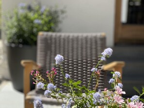 A wicker chair with a woven backrest, positioned outdoors with a blurred background of greenery and a building. - Alluring Family Chalet in Wagrain with Sauna near City Center (Wagrain)