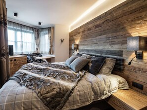 A bedroom with a wooden headboard, a bed with plaid bedding, a desk, and a window with curtains. - Alluring Family Chalet in Wagrain with Sauna near City Center (Wagrain)