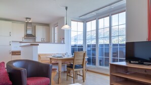 A modern living room with a sofa, a dining table, and a TV on a wooden stand. - Modern Apartment in St Margarethen With Mountain View (Sankt Margarethen im Lungau)