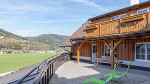 A wooden chalet with a balcony overlooking a green field and mountains. - Modern Apartment in St Margarethen With Mountain View (Sankt Margarethen im Lungau)