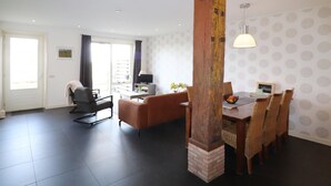 Ein modernes Wohnzimmer mit einer Couch, einem Esstisch mit Stühlen, einem Fernseher und einer großen Holzsäule.