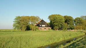 Ein Haus mit schrägem Dach, umgeben von einem Feld und Bäumen.