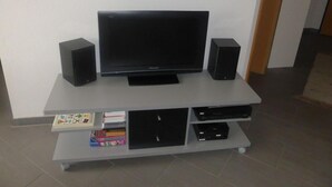 A flat-screen TV on a white entertainment center with two speakers, a shelf with books and a remote control, and a small table with children's books. - Luxurious Chalet in Habkern With Private Garden (Habkern)