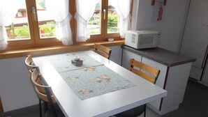 A small kitchen with a white table, wooden chairs, a microwave, and a window with curtains. - Luxurious Chalet in Habkern With Private Garden (Habkern)