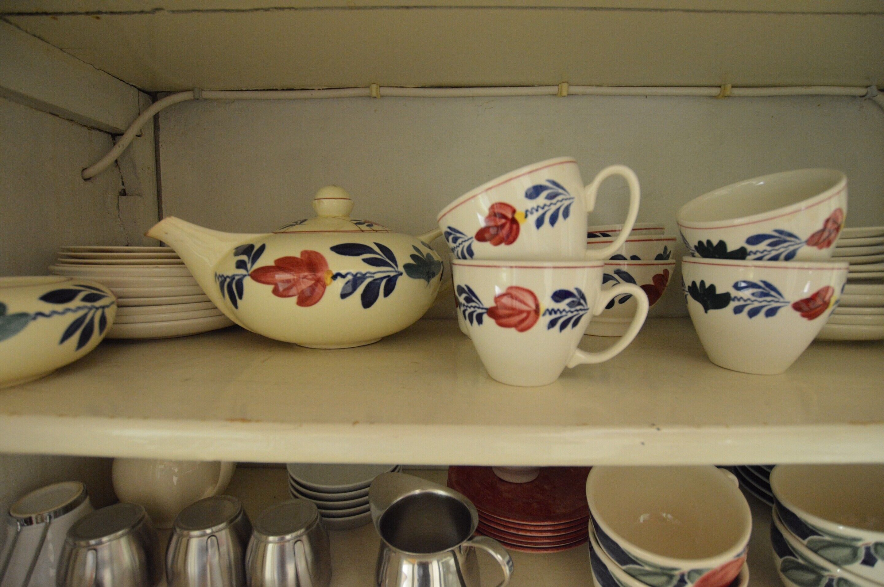 A shelf with various ceramic items including teapots, cups, and saucers, some with floral designs.