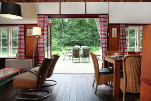 A wooden-floored room with wicker furniture, a dining table, and chairs. - Cozy Holiday Home near Forest in Zuidwolde (Zuidwolde)