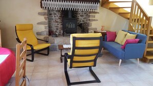 Una sala de estar acogedora con una chimenea de piedra, dos sillones amarillos, un sofá azul y una escalera de madera.